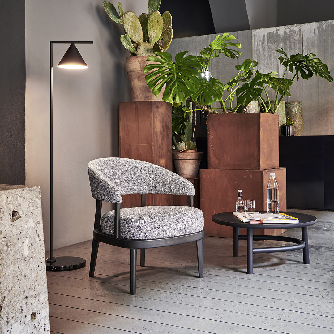 Gray upholstered chair with a textured pattern, surrounded by earthy brown planters and lush green plants.