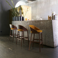 Stylish bar stools with curved wooden frames and mustard yellow cushions against a modern concrete bar.