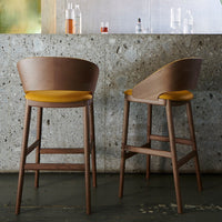 Brown wooden bar stools with yellow seats, featuring a smooth curved back and minimalistic design against a textured background.