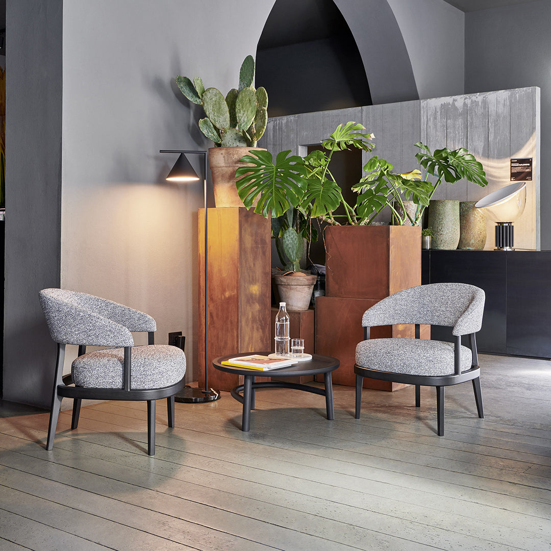 Stylish grey upholstered chairs with rounded backs, set against a modern backdrop and lush greenery.
