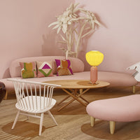 Modern pastel pink lounge with colorful patterned pillows, creamy white chair, and vibrant yellow lamp.