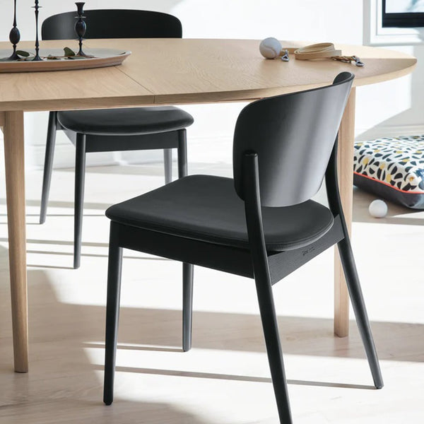 Black minimalist chair with sleek lines against a light wooden table, featuring a modern, elegant design.