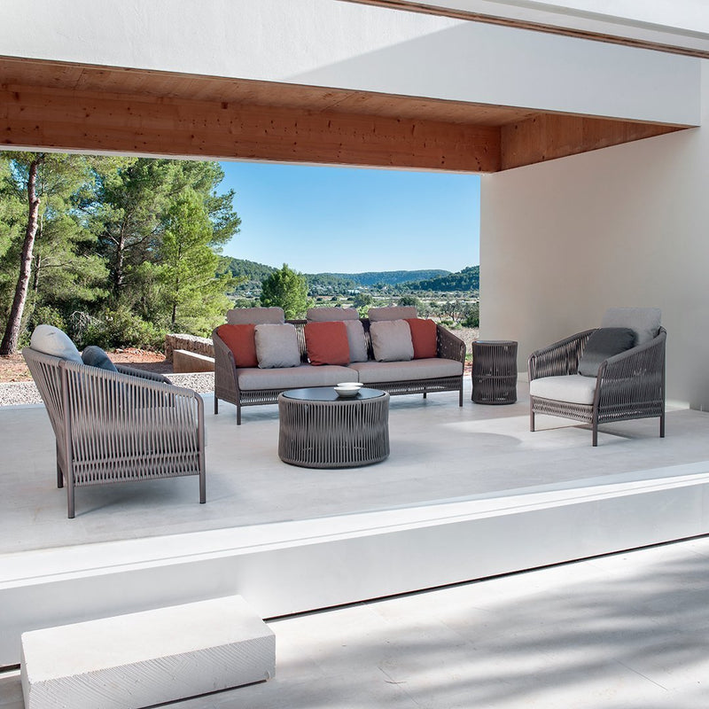 Modern outdoor seating set featuring gray wicker, soft beige cushions, and coral accent pillows against a scenic backdrop.