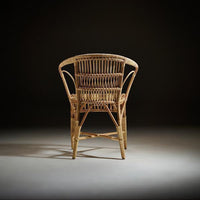 Natural rattan chair with intricate woven patterns, featuring a warm tan hue against a dark background.