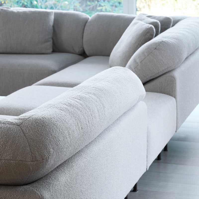 Light gray sectional sofa with textured fabric and soft curves, featuring minimalist design and neutral tones.