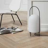 Minimalist white lamp with ribbed texture and sleek black stand, set against warm wooden herringbone floor.