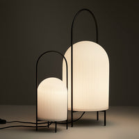 Black frame arch lamps with ribbed white shades, showcasing a modern minimalist design in warm lighting.