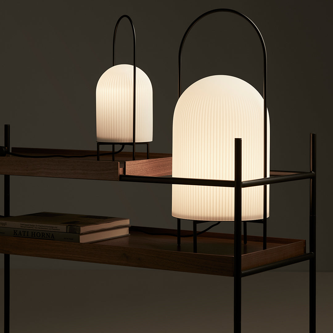 "Two modern lamps with curved white glass shades and black metal frames on a wooden shelf, featuring a minimalist design."