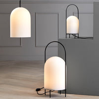 Minimalist white lamp with an arched design, featuring a soft glow against a sleek black frame and light-colored background.