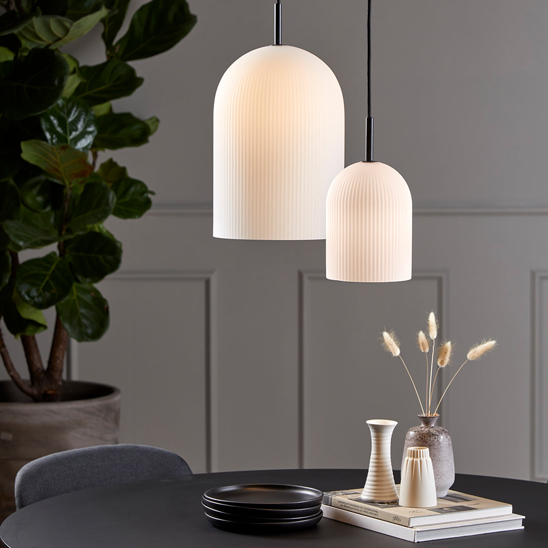 Modern pendant lamps in white with ribbed texture, hanging above a neutral-toned table setting with greenery.
