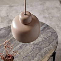 "Round beige pendant light with a smooth matte finish, hanging over a textured gray stone table."