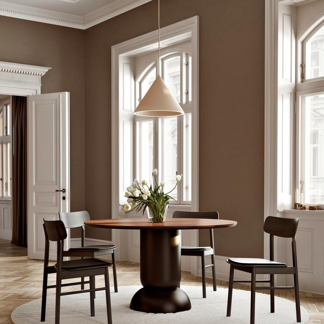 Minimalist dining room with a round wooden table, black chairs, cream walls, and a light beige pendant lamp.