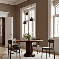 Modern dining room with brown walls, dark chairs, wooden table, and white flowers, creating a warm, elegant atmosphere.