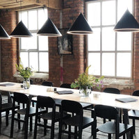 Modern dining setup featuring black cone pendant lights, warm brick walls, and a sleek white table. Green floral accents.