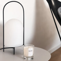 White lamp with ribbed texture on a black metal stand, paired with a clear glass candle on a round table.