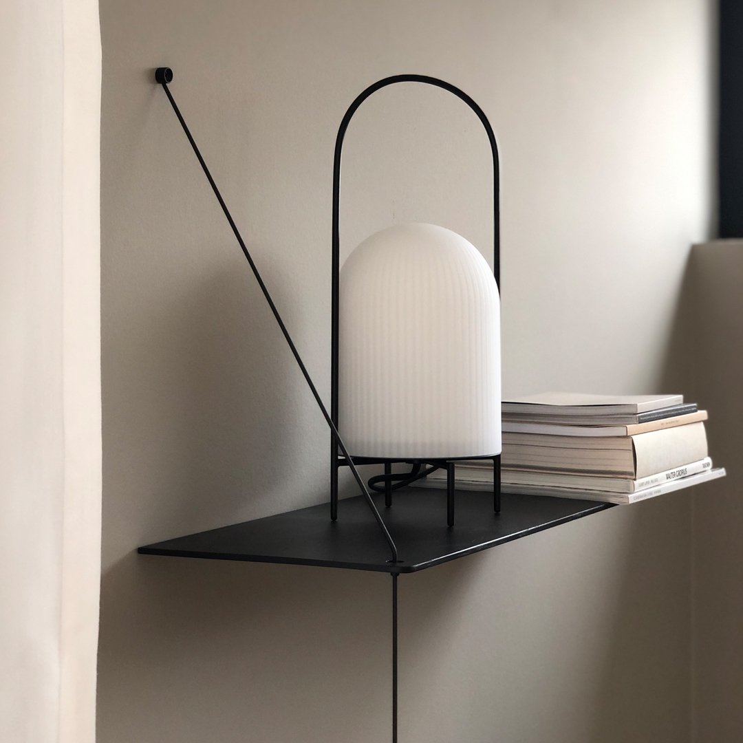 Modern black shelf lamp with a white ribbed glass shade, minimalist design against a neutral wall.