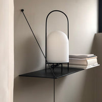 Modern black shelf lamp with a white ribbed glass shade, minimalist design against a neutral wall.