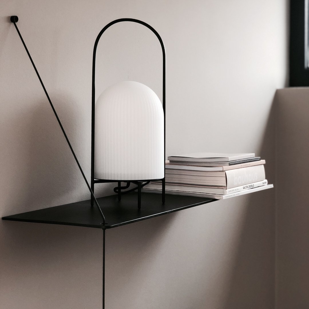 Minimalist black metal shelf with a sleek white lamp and stacked gray books, creating a modern decor aesthetic.