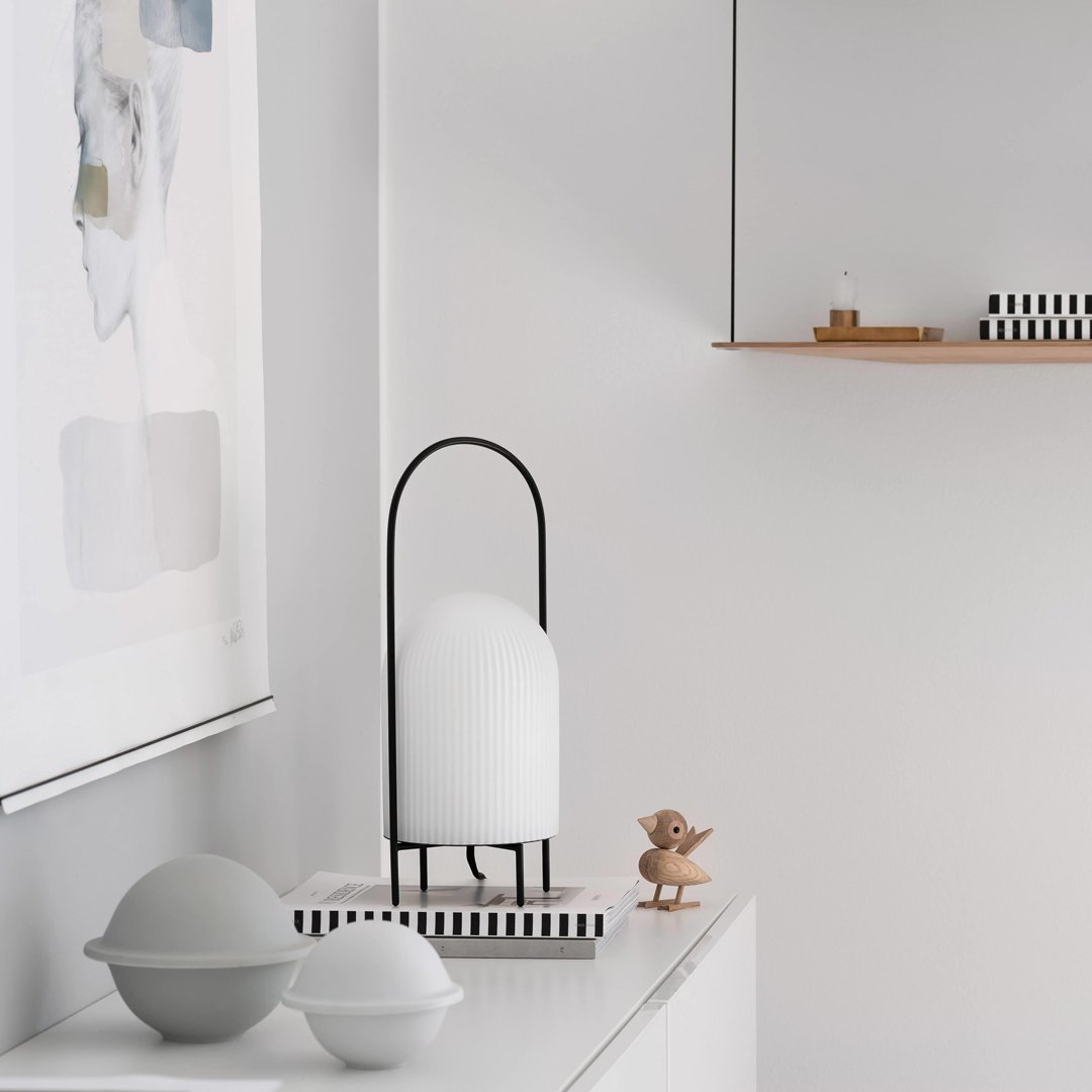 Minimalist decor featuring a white lamp with black accents, striped base, and grey bowls on a light background.