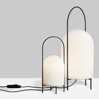 "Pair of modern lamps with white ribbed shades and black metal frames against a gray background."