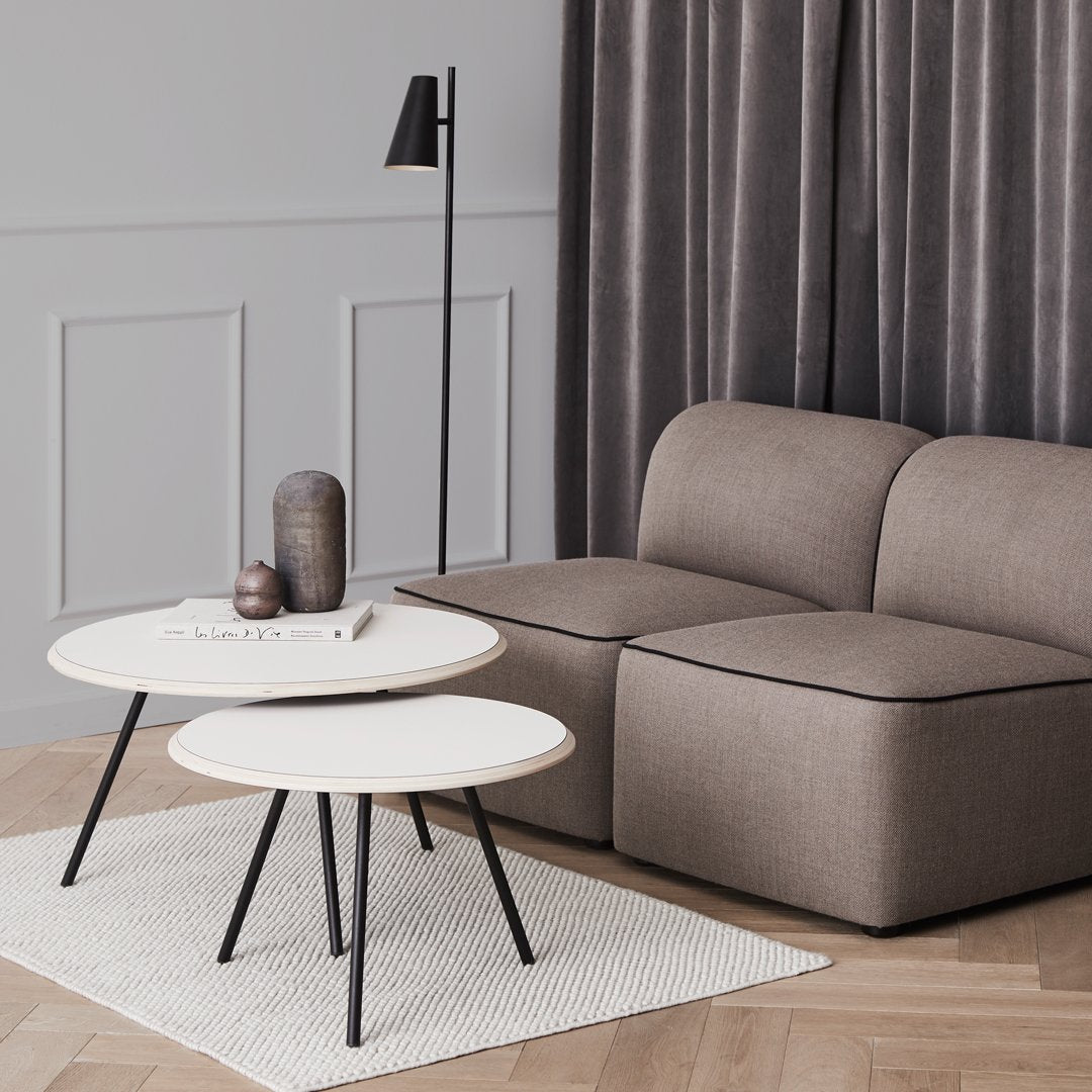 Modern coffee tables with white tops and black legs, complemented by a cozy beige sofa and gray curtains.