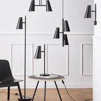 Black modern lamps and a round table with a dark top, set against a light wall with wooden flooring.