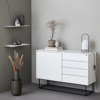 Modern white cabinet with black metal legs, displayed against a soft gray wall, accented by neutral decor and earthy tones.