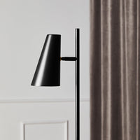 Black modern lamp with a sleek cone shade against a soft gray backdrop and elegant curtains.