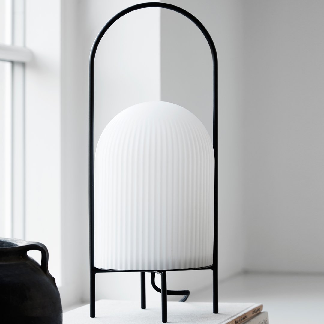White ribbed lamp with a black metal frame, featuring a modern minimalist design and sleek lines.
