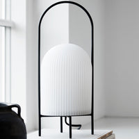 White ribbed lamp with a black metal frame, featuring a modern minimalist design and sleek lines.