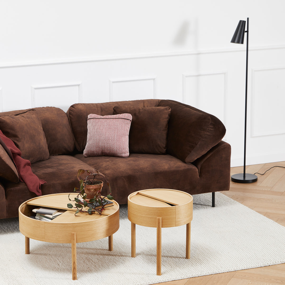 Brown suede couch with a pink accent pillow, paired with wooden tables on a neutral rug and light wood floor.