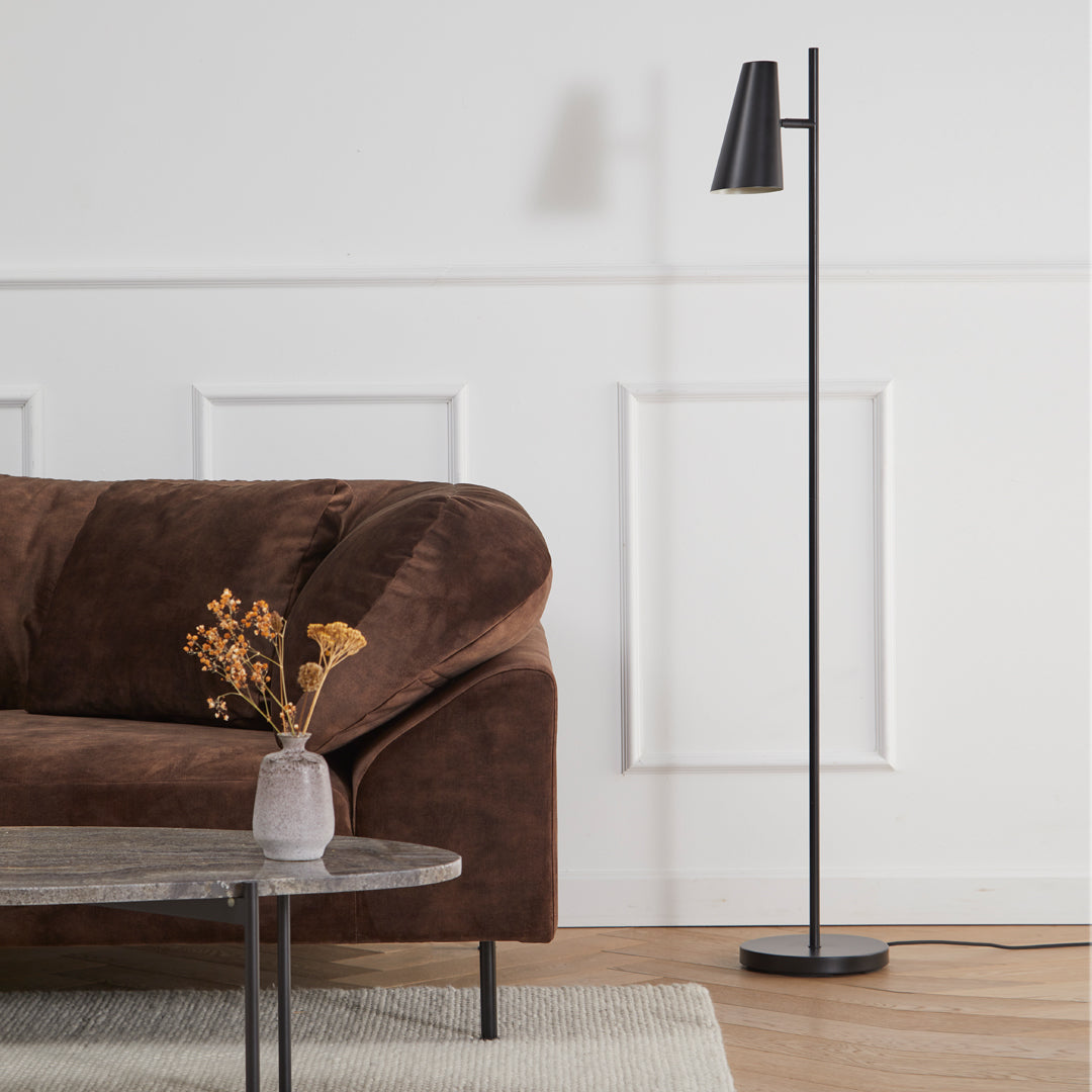 Brown velvet sofa with a sleek black floor lamp; minimalist design against a light-colored wall. Modern decor.