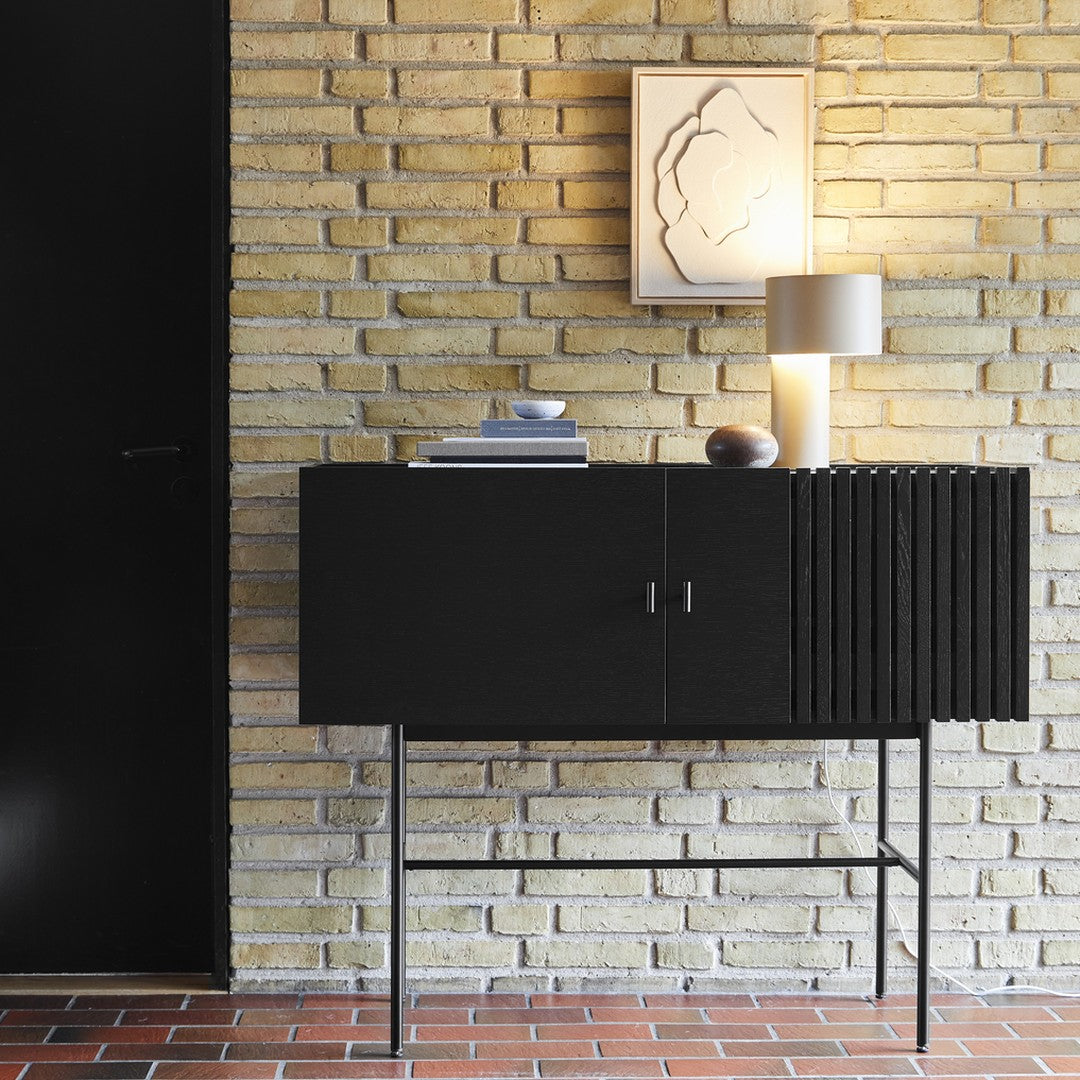 Black wooden cabinet with sleek lines, set against textured yellow brick wall and warm light tones.