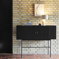 Black wooden cabinet with sleek lines, set against textured yellow brick wall and warm light tones.