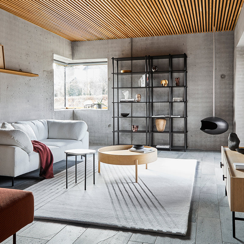 Modern living room featuring a white sofa, earthy tones, wooden ceiling, and a circular wood coffee table on a light rug.