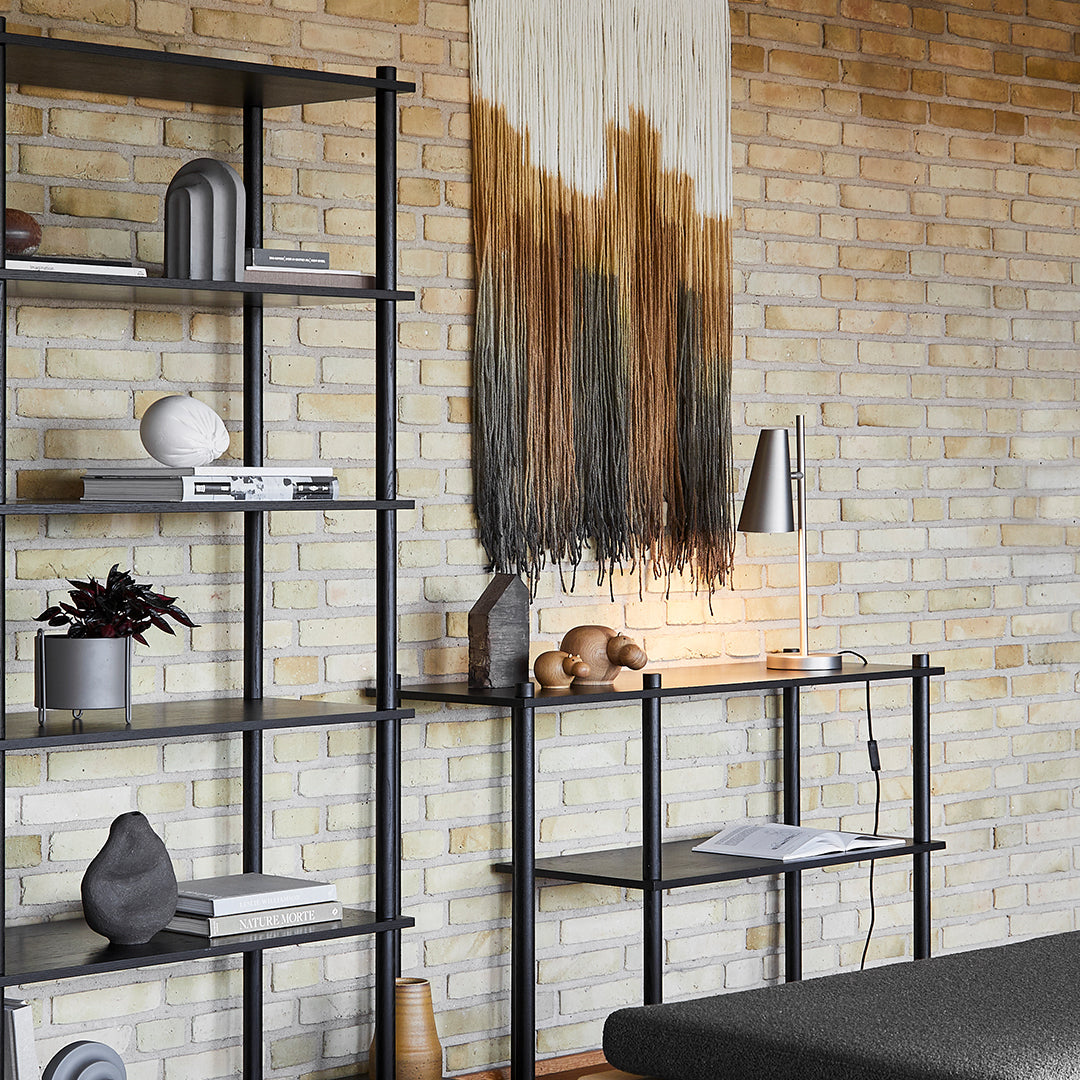 Modern shelf with black metal frame and neutral decor, featuring earthy tones and textured wall hanging in warm hues.