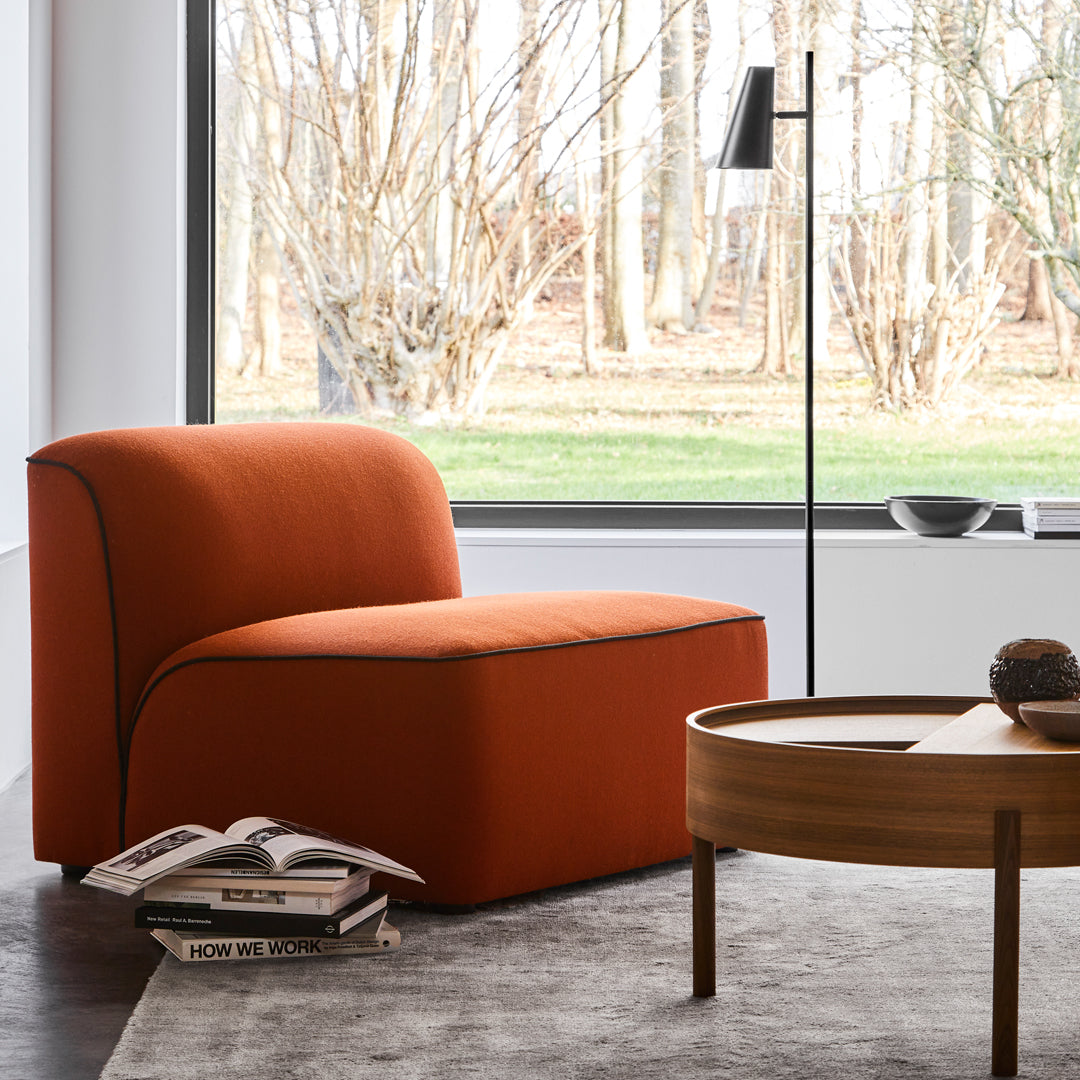 Rust-orange modern chair with minimalistic design and contrasting dark trim, complemented by a cozy gray rug.