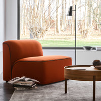 Rust-orange modern chair with minimalistic design and contrasting dark trim, complemented by a cozy gray rug.