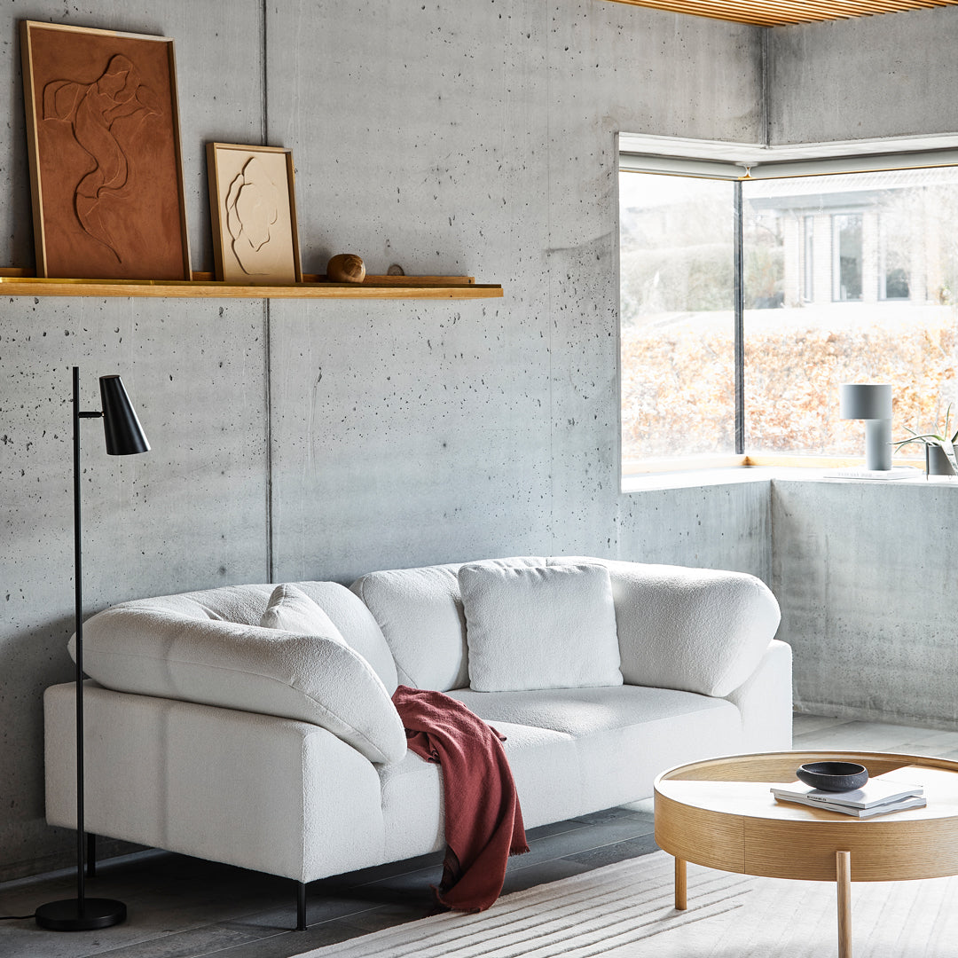 Stylish white modern sofa with a deep red throw, complemented by a textured gray rug and light wooden coffee table.
