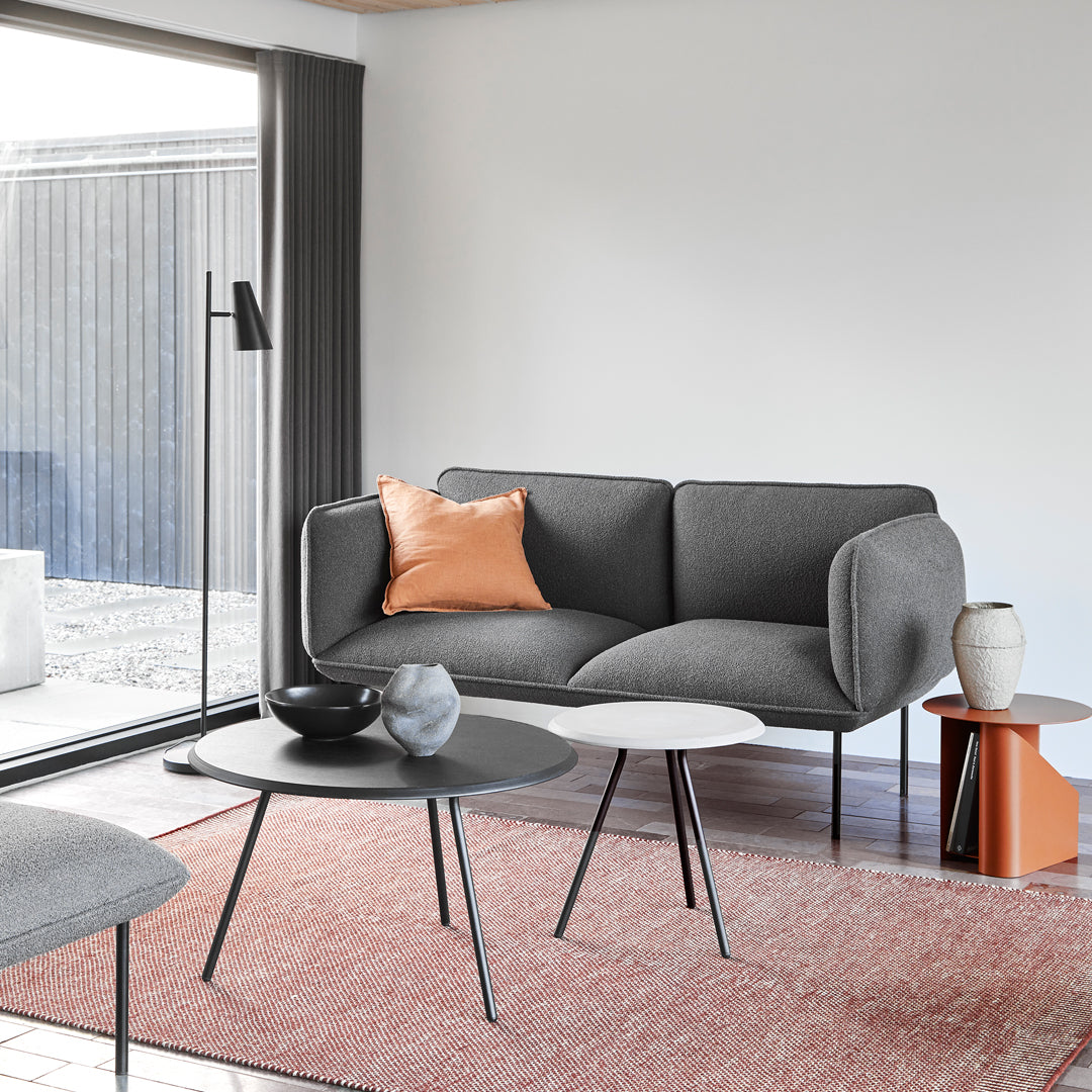 Gray fabric sofa with an orange accent cushion, paired with black and white tables on a textured pink rug.