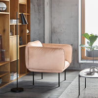 Soft pink velvet armchair with sleek black metal legs, set against a minimalist interior backdrop.