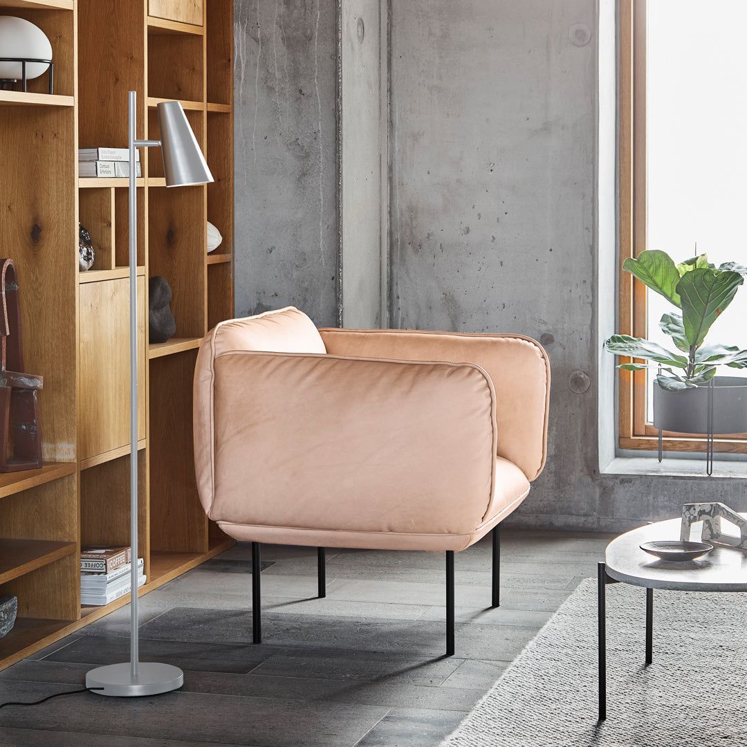 Soft blush pink velvet armchair with a minimalist design, paired with natural wood and gray tones in a modern setting.