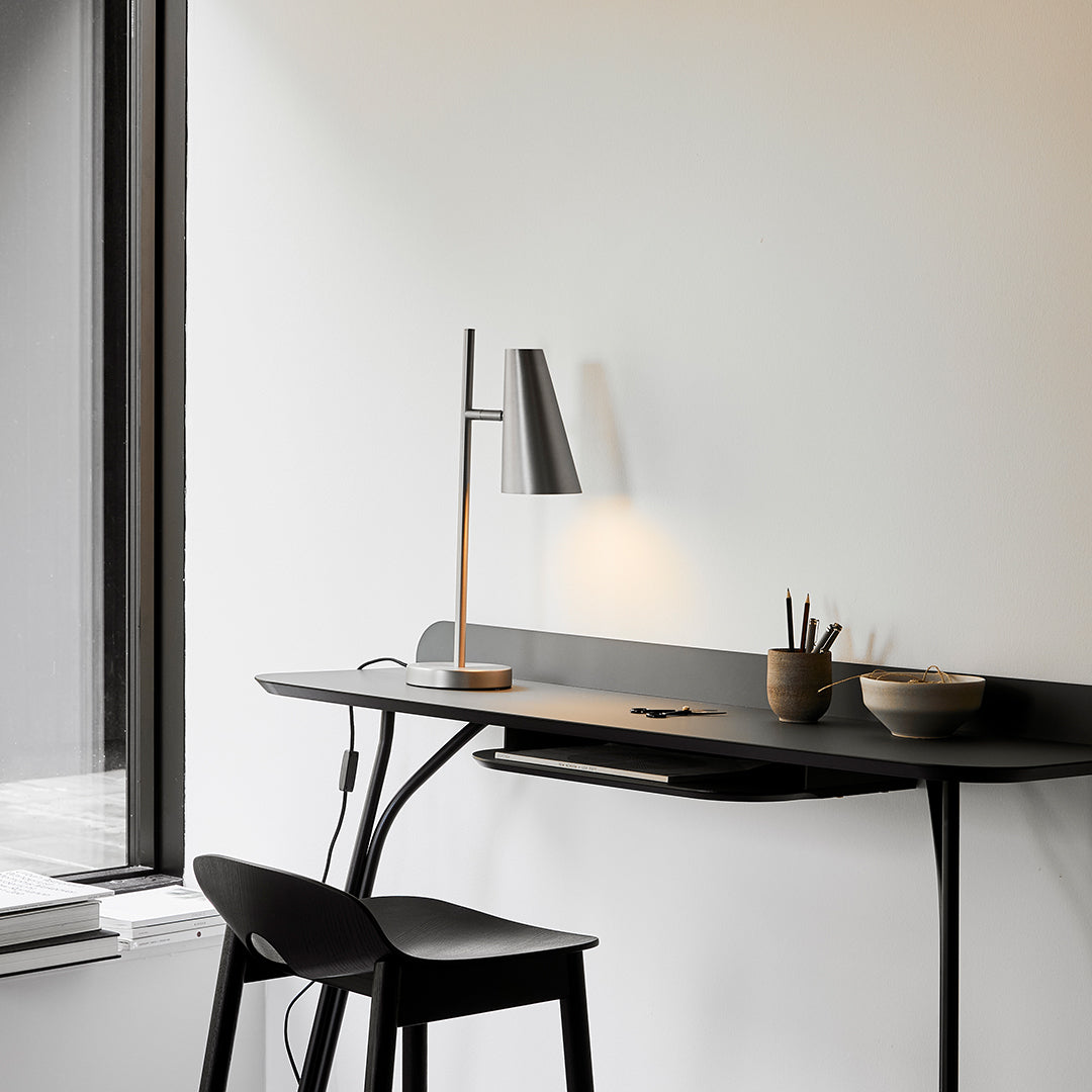 Minimalist black desk with sleek lines, paired with a matching black stool in a modern, neutral room setting.