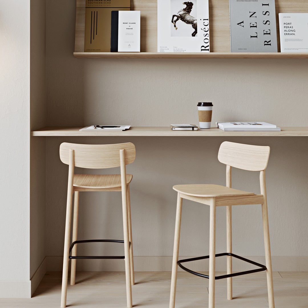 "Minimalist natural wood bar stools with soft beige tones against a light gray wall and wooden shelf decor."
