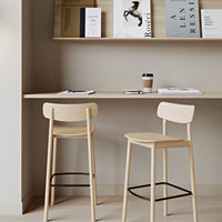 "Minimalist natural wood bar stools with soft beige tones against a light gray wall and wooden shelf decor."