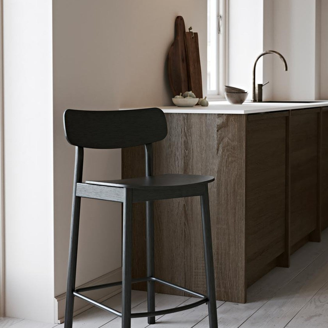 Black wooden bar stool against a warm neutral wall and wood grain cabinetry, showcasing modern minimalism in color and design.