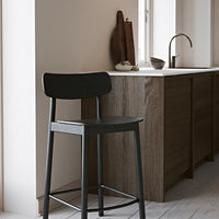 Black wooden bar stool against a warm neutral wall and wood grain cabinetry, showcasing modern minimalism in color and design.
