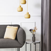 Gray sofa with a yellow patterned cushion, gray curtains, and yellow hanging lamps add vibrant color to a minimalist decor.