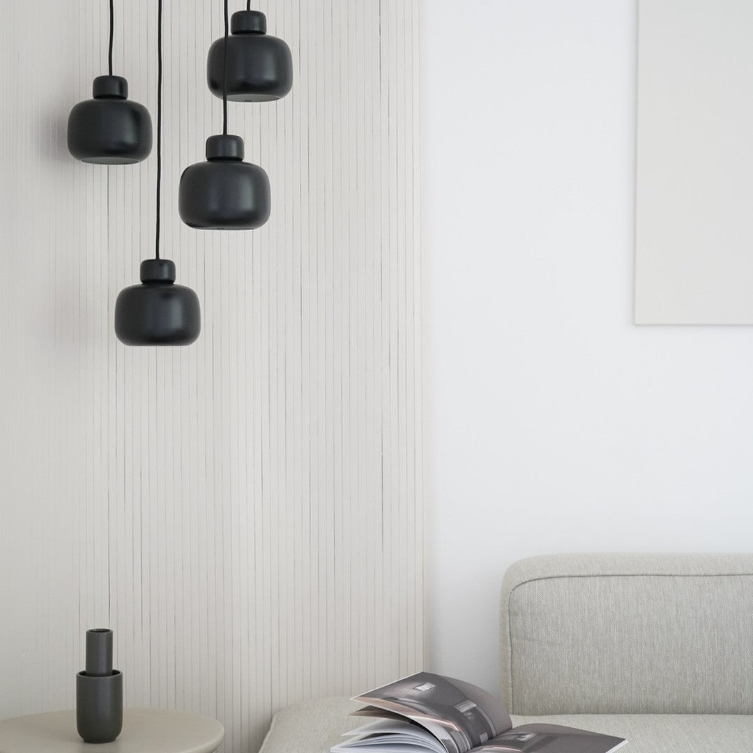 "Four matte black pendant lights hang against a textured white wall, complementing neutral tones in the modern space."