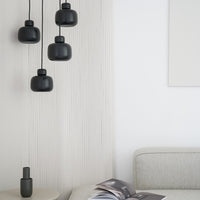 "Four matte black pendant lights hang against a textured white wall, complementing neutral tones in the modern space."